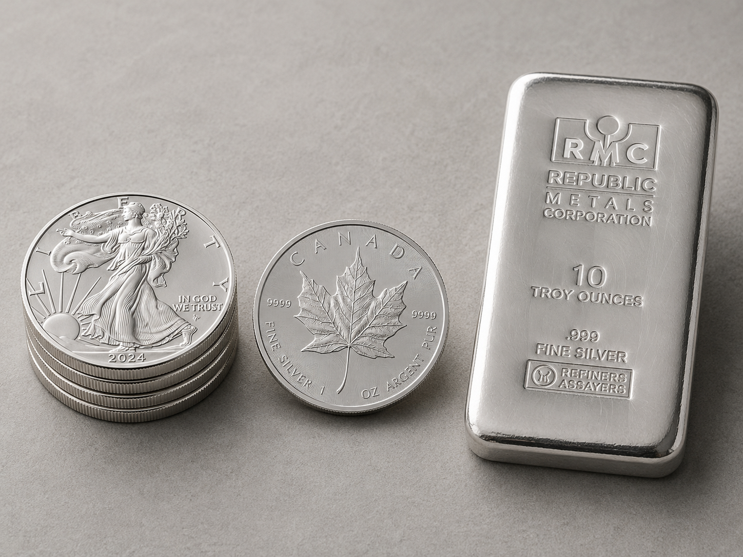 American Silver Eagle, Canadian Silver Maple Leaf, and a 10 oz silver bar — three of the most common IRA-eligible silver bullion products — on a neutral surface.